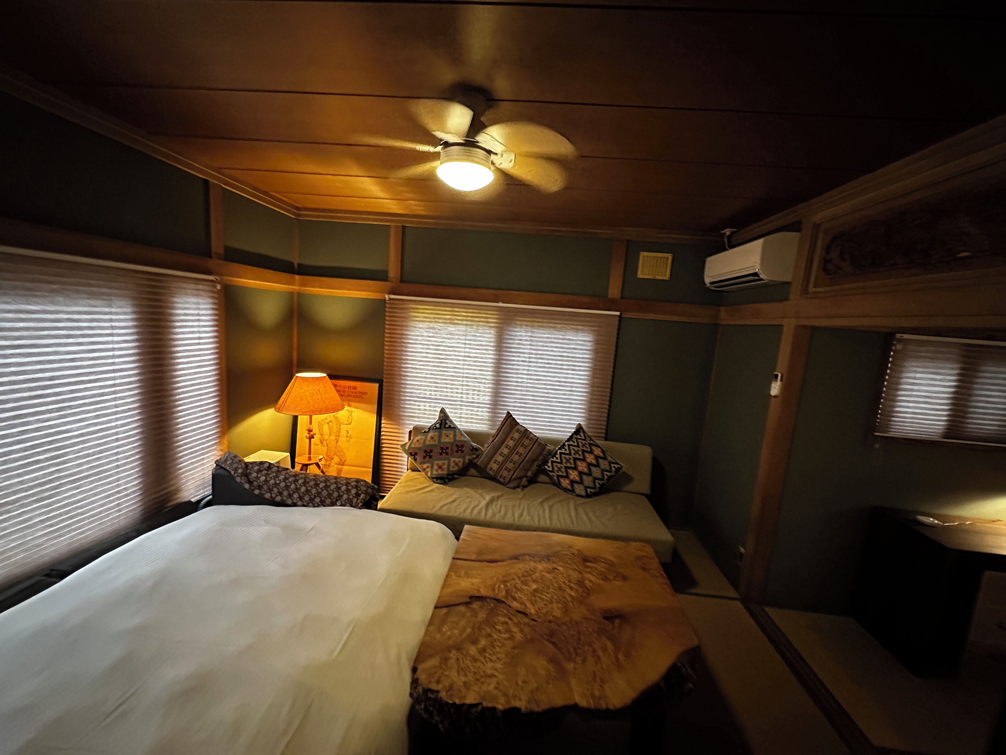 Une chambre avec deux lits, un ventilateur de plafond, une lampe et une fenêtre avec des stores.