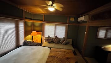 Une chambre avec deux lits, un ventilateur de plafond, une lampe et une fenêtre avec des stores.
