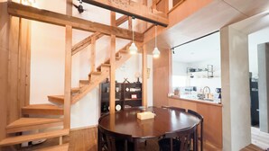 A wooden interior with a staircase, a round dining table, and a kitchen area. - The Cozy Nest MATSUKAWA (Hakodate)