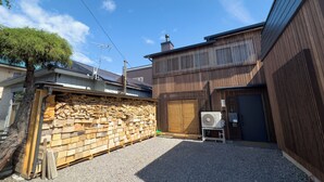A residential area with a gravel driveway, wooden fences, and a stack of firewood. - The Cozy Nest MATSUKAWA (Hakodate)