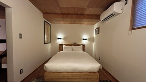 A bedroom with a wooden headboard, a bed with white bedding, two wall-mounted lights, and an air conditioning unit. - The Cozy Nest MATSUKAWA (Hakodate)