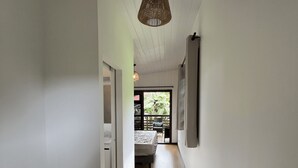 A hallway with wooden flooring, white walls, and a ceiling with a hanging light fixture. - Hava'i Lodge (Raiatea)
