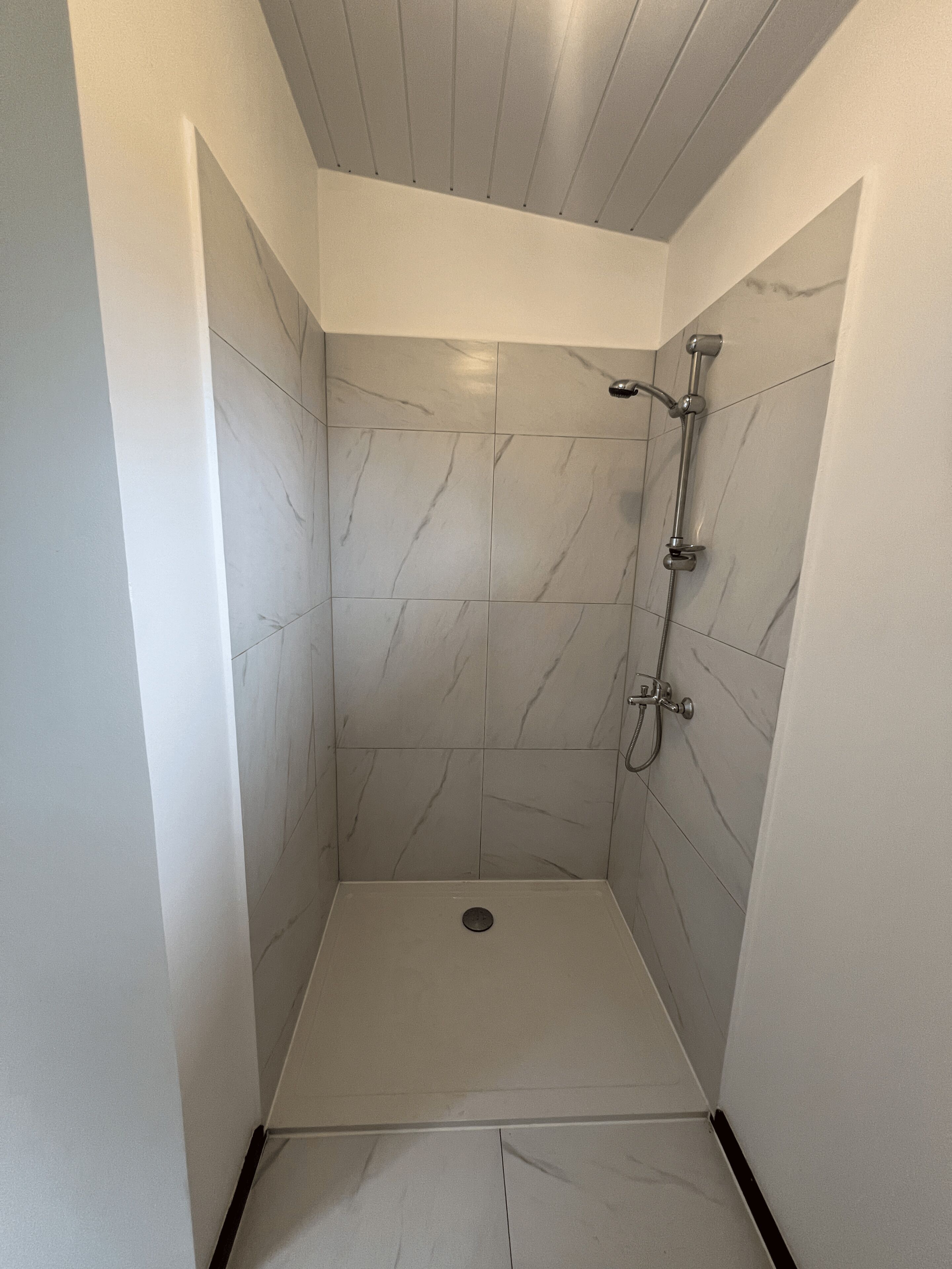 Un espacio de ducha pequeño y cerrado con piso y paredes de azulejos, un cabezal de ducha manual y un grifo instalado en la pared.