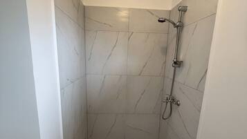 Un espacio de ducha pequeño y cerrado con piso y paredes de azulejos, un cabezal de ducha manual y un grifo instalado en la pared.