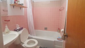 A bathroom with a toilet, sink, and bathtub. There is a shower curtain, a shelf with toiletries, and a door.