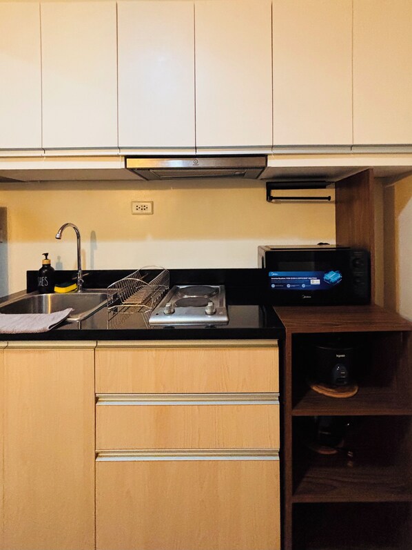 A compact kitchen with a sink, a dish rack, a small stove, and a microwave. - A Dreamy & Elegant Studio (Iloilo)
