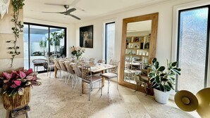 A spacious dining area with a large table set for six, surrounded by chairs. There is a ceiling fan, large windows, and a mirror on the wall. - Stunning beach house overlooking North Curl Curl beach (North Curl Curl)