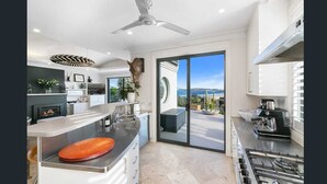 A modern kitchen with a large island, a built-in oven, and a view of the outdoors. - Stunning beach house overlooking North Curl Curl beach (North Curl Curl)