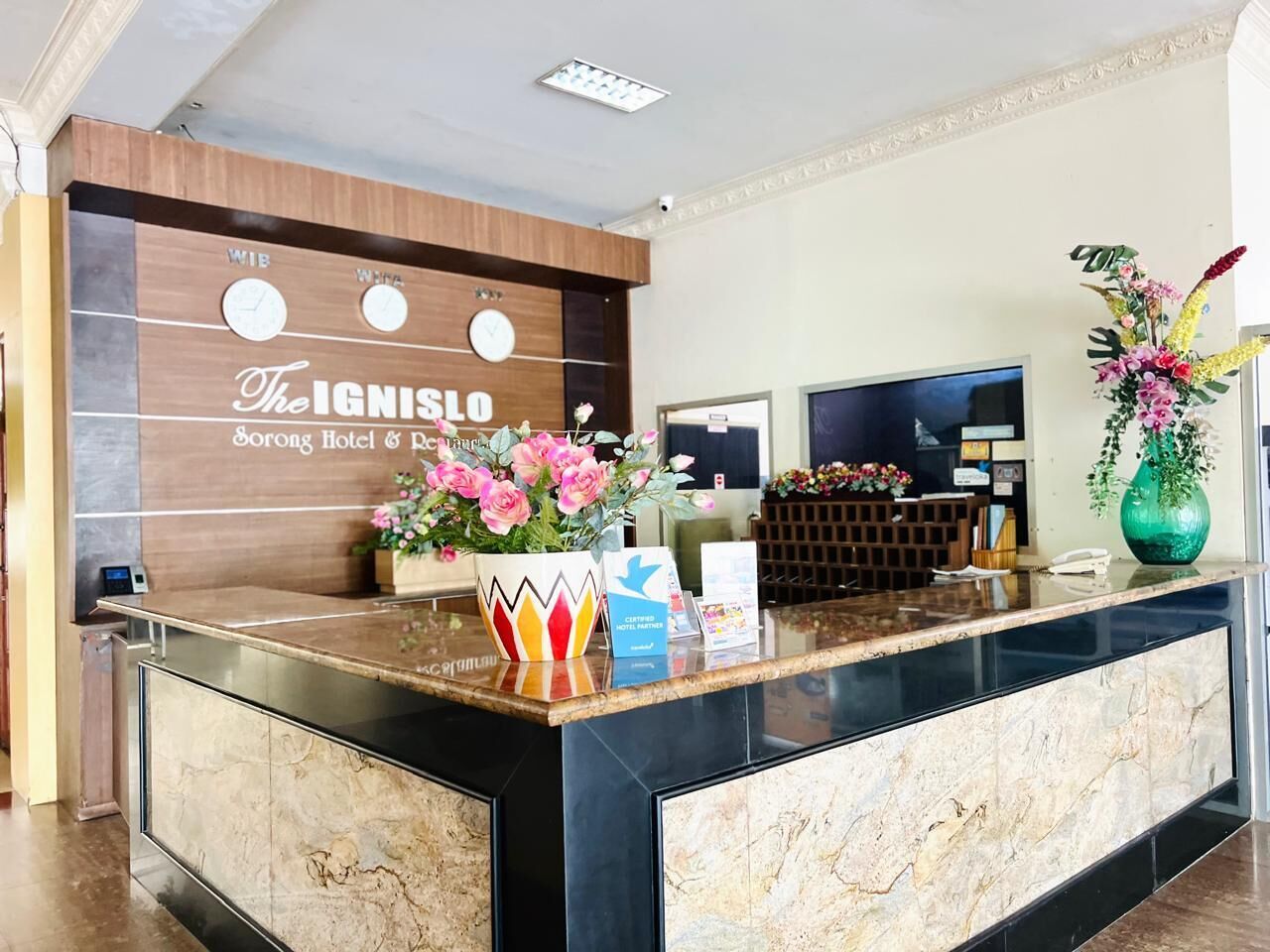 A hotel reception desk with a marble counter, a clock, and a flower vase.