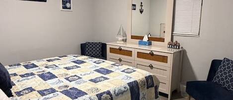 A bedroom with a bed, dresser, and a ceiling fan. There is a sign on the wall that says "Welcome to our Beach House."