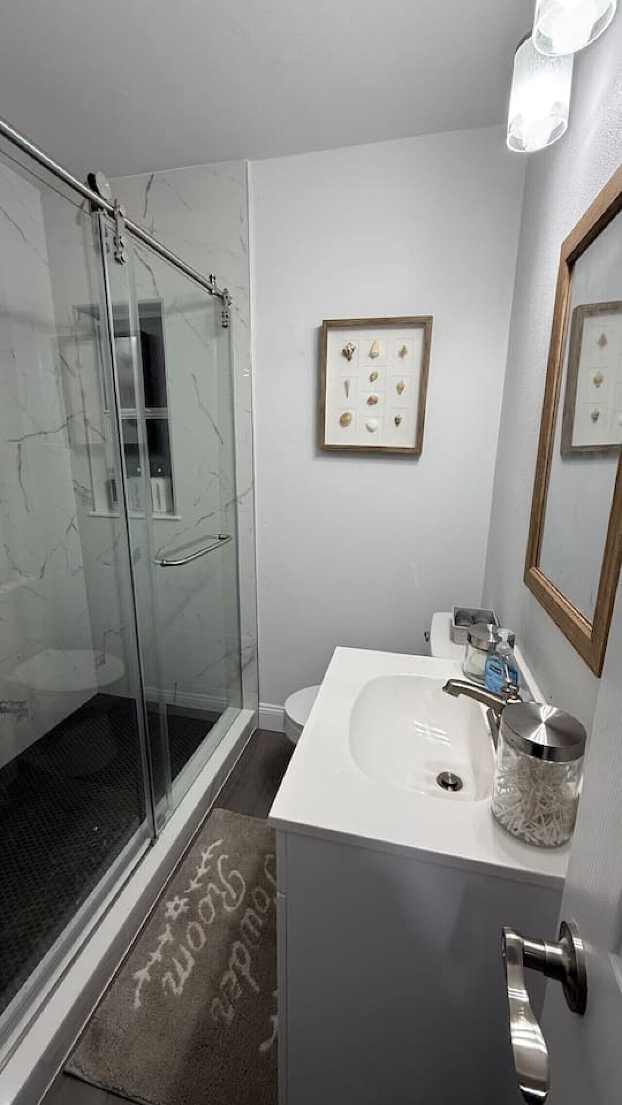 A bathroom with a glass shower enclosure, a white sink with a stainless steel faucet, and a framed picture on the wall.