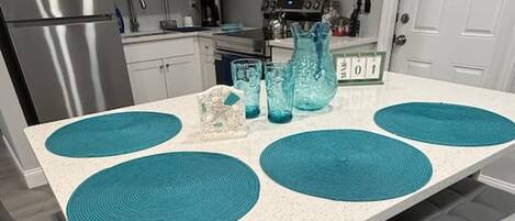 A modern kitchen with white cabinets, stainless steel appliances, and a central island with teal placemats.