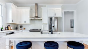 Una cocina moderna con armarios blancos, un refrigerador de acero inoxidable y una isla central con taburetes de bar.