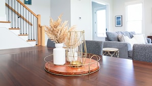 Una mesa de comedor de madera con un jarrón blanco y una cesta de alambre dorada con plantas secas.