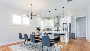 Una cocina moderna con armarios blancos, un refrigerador de acero inoxidable y una zona de comedor con una mesa grande y sillas.