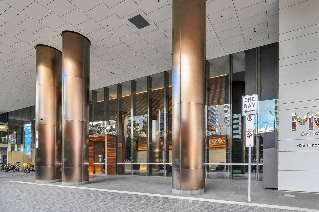 A modern building entrance with large cylindrical columns, glass doors, and a "ONE WAY" sign.