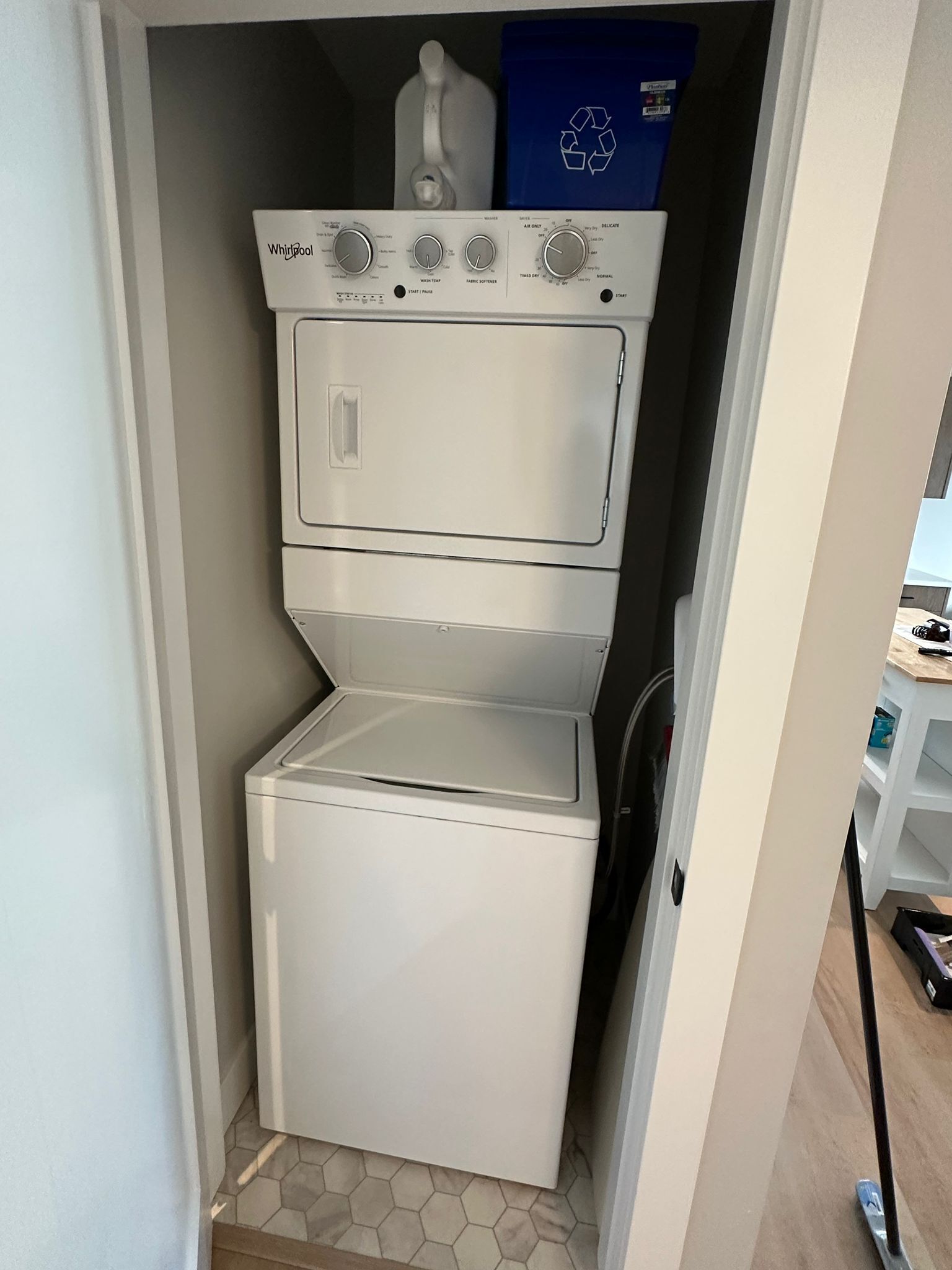 A compact, white Whirlpool washer and dryer unit in a small laundry room with a tiled floor.