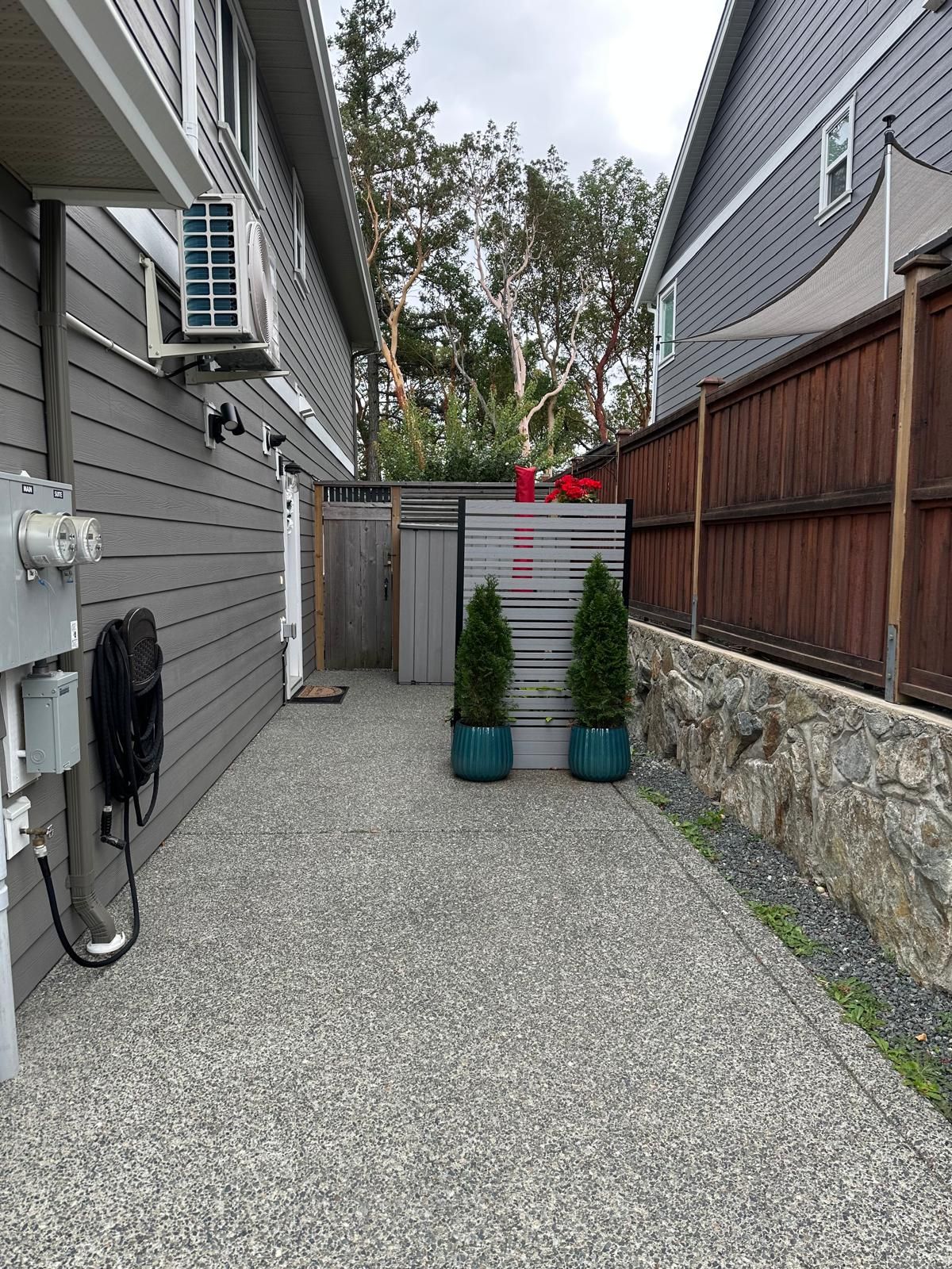 A residential outdoor area with a gravel driveway, a wooden fence, and a small garden with potted plants.