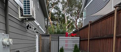 A residential outdoor area with a gravel driveway, a wooden fence, and a small garden with potted plants.