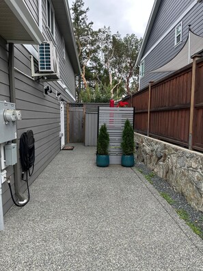 A residential outdoor area with a gravel driveway, a wooden fence, and a small garden with potted plants. - Modern One-Bedroom Retreat in Bear Mountain (Langford)
