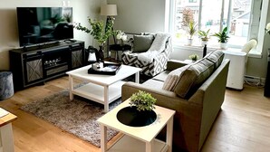 A modern living room with a sofa, coffee table, and TV. There are potted plants and a window providing natural light. - Modern One-Bedroom Retreat in Bear Mountain (Langford)