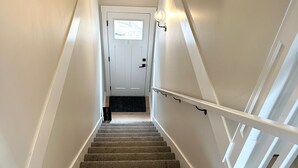 A carpeted staircase with white railings leading to a door with a window. - Modern One-Bedroom Retreat in Bear Mountain (Langford)