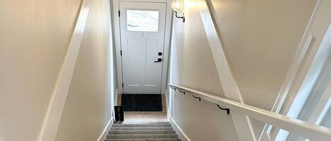A carpeted staircase with white railings leading to a door with a window.