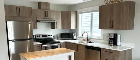 Una cocina moderna con armarios de madera, electrodomésticos de acero inoxidable, una encimera blanca y un cartel que dice 'Bienvenido'.