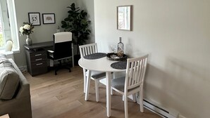 A dining area with a white table and chairs, a grey sofa, and a small side table with a vase. - Modern One-Bedroom Retreat in Bear Mountain (Langford)