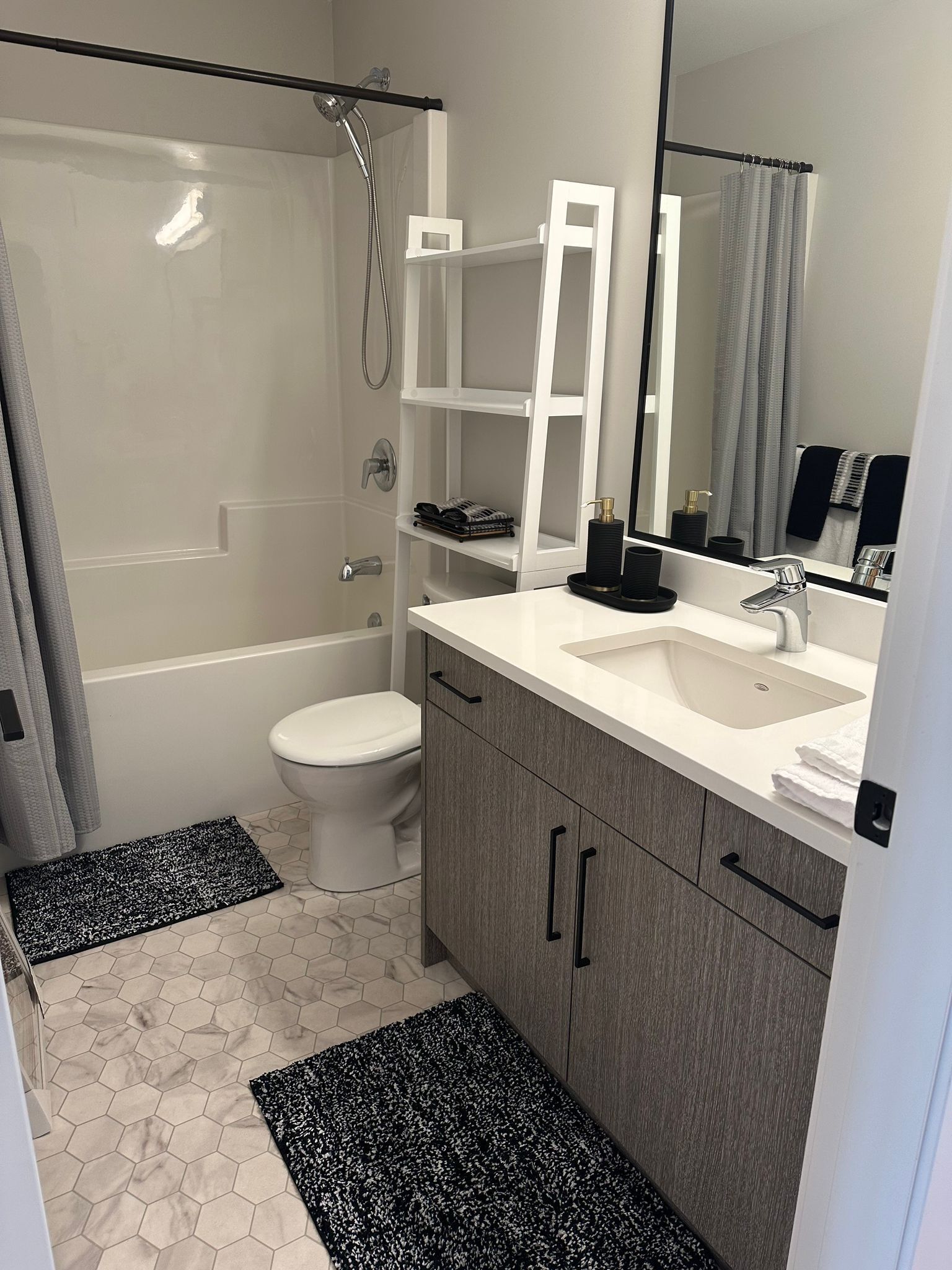 A modern bathroom with a bathtub, toilet, and sink. There are black and white patterned mats on the floor.
