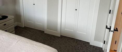 A bedroom with a bed, two white wardrobes, a bedside table, and a carpeted floor.