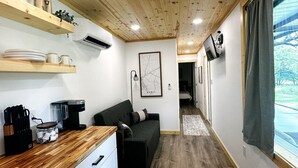 A compact living space with a kitchenette, a sofa, a map on the wall, and a window with a view of trees.