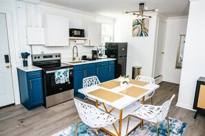 Eine moderne Küche mit blauen Schränken, weißen Arbeitsplatten und einem Essbereich mit einem weißen Tisch und Stühlen.