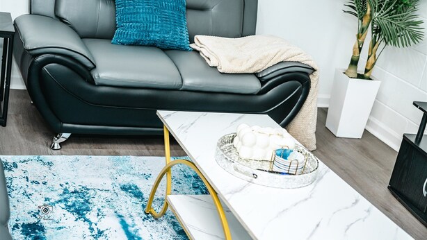 Un salon moderne avec un canapé en cuir gris, une table basse en marbre blanc et un tapis à motifs bleus.