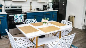 Une cuisine moderne avec des meubles blancs, un réfrigérateur noir et une table à manger avec des chaises blanches.