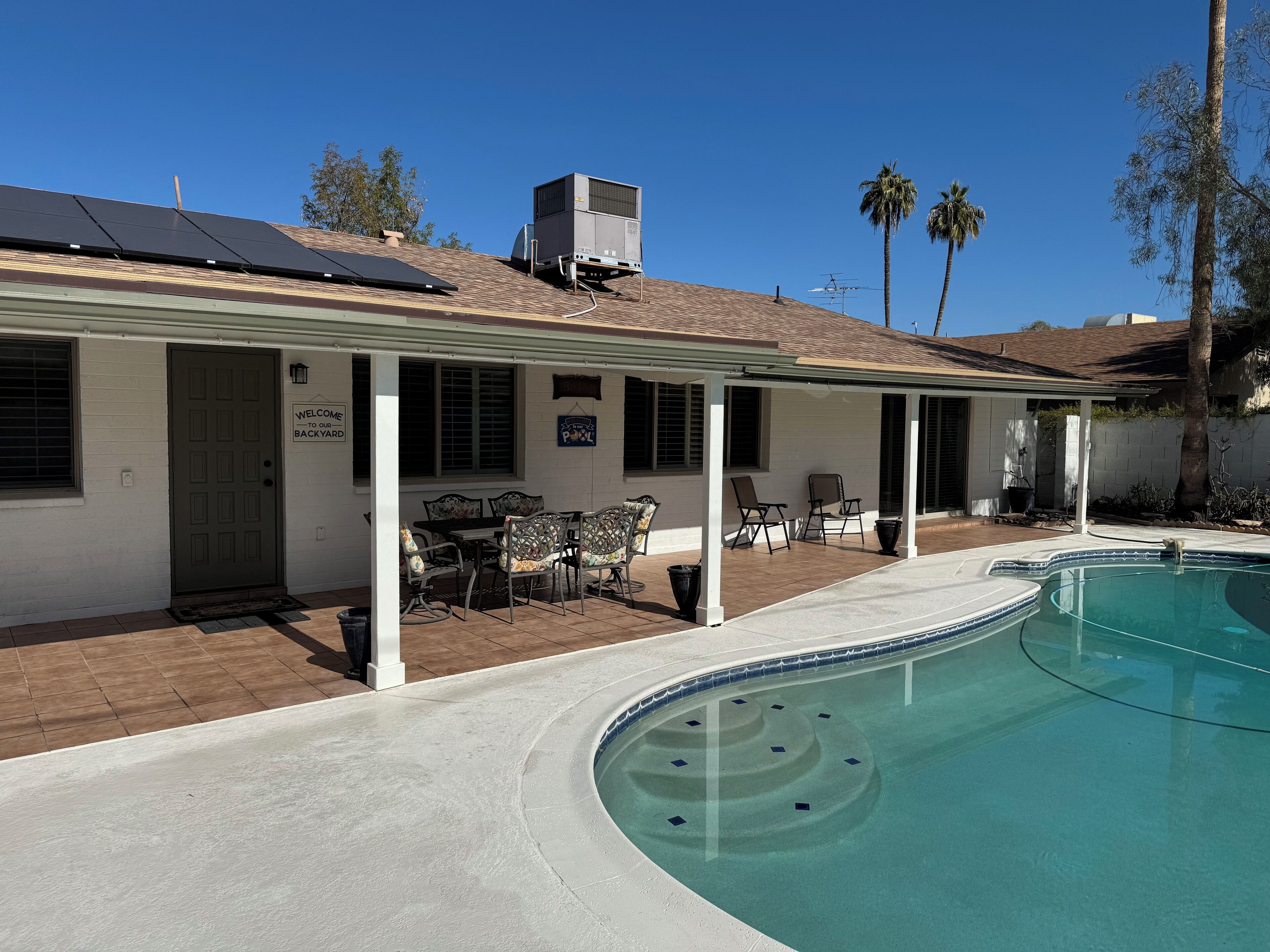 A residential property with a swimming pool, patio furniture, and solar panels on the roof.