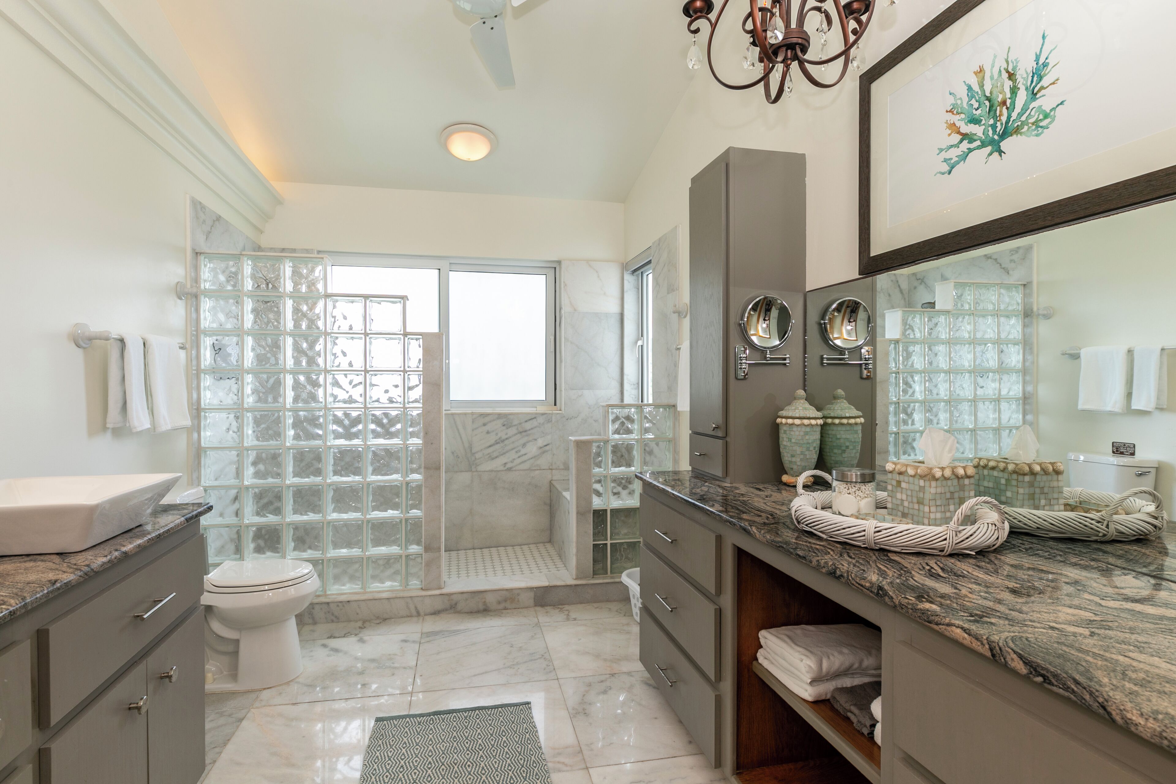 A modern bathroom with a glass shower enclosure, marble flooring, and a large mirror with decorative jars.