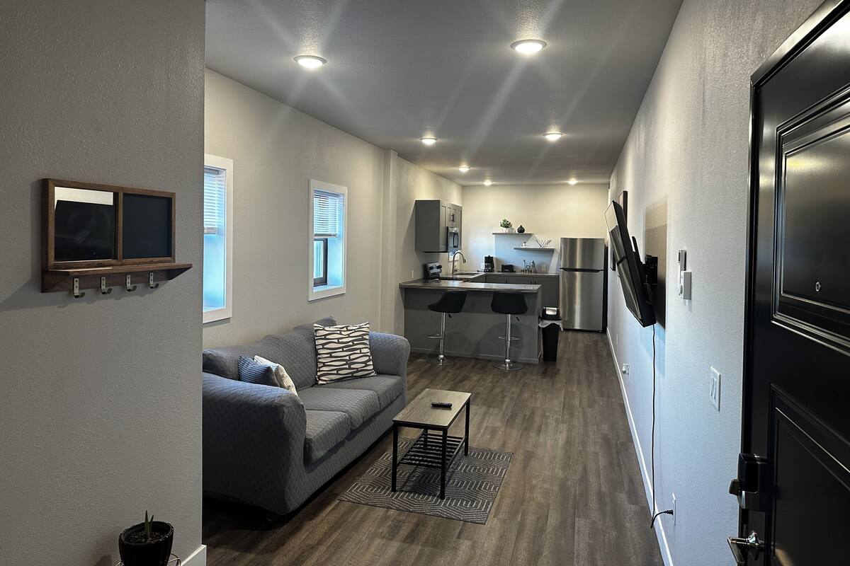 A compact living space with a kitchenette, grey walls, a sofa, and a small table.
