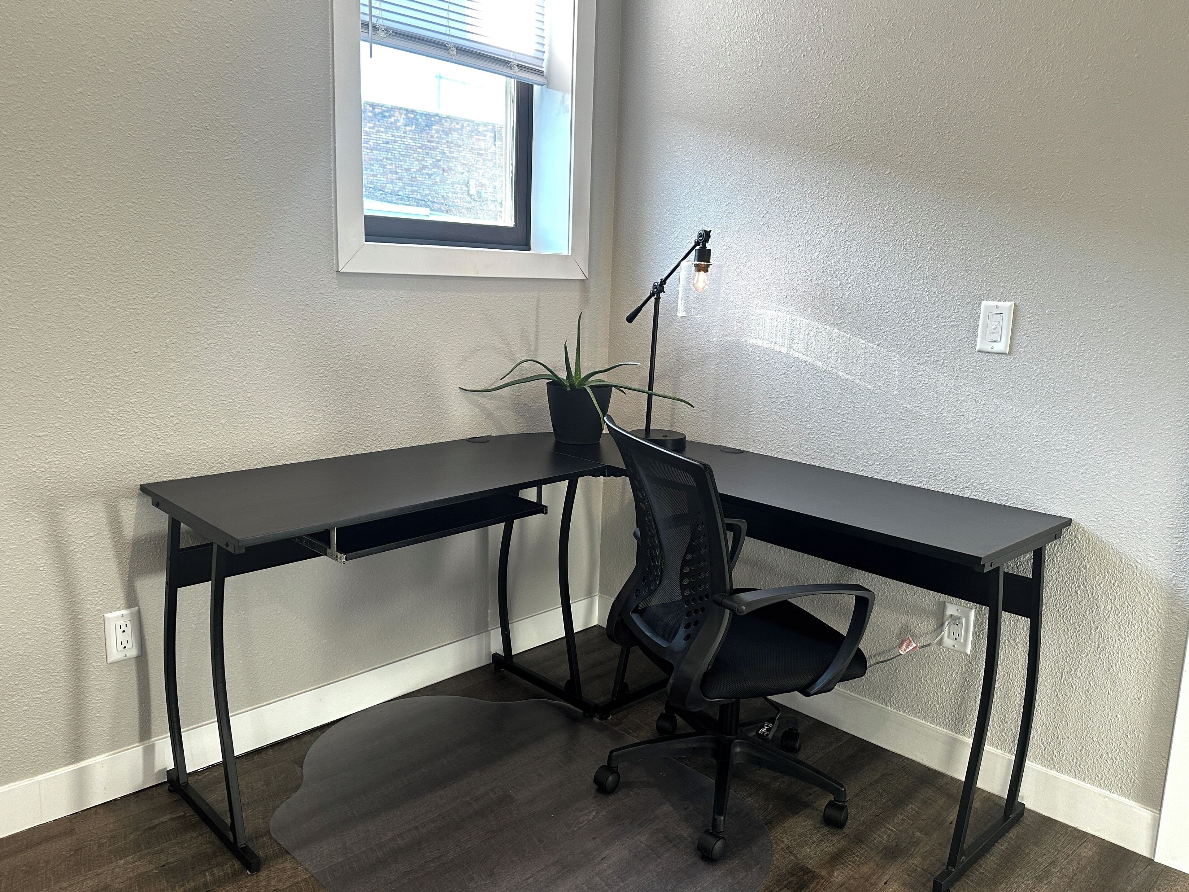 Un bureau d’angle avec un bureau noir, une chaise de bureau noire et une plante en pot.