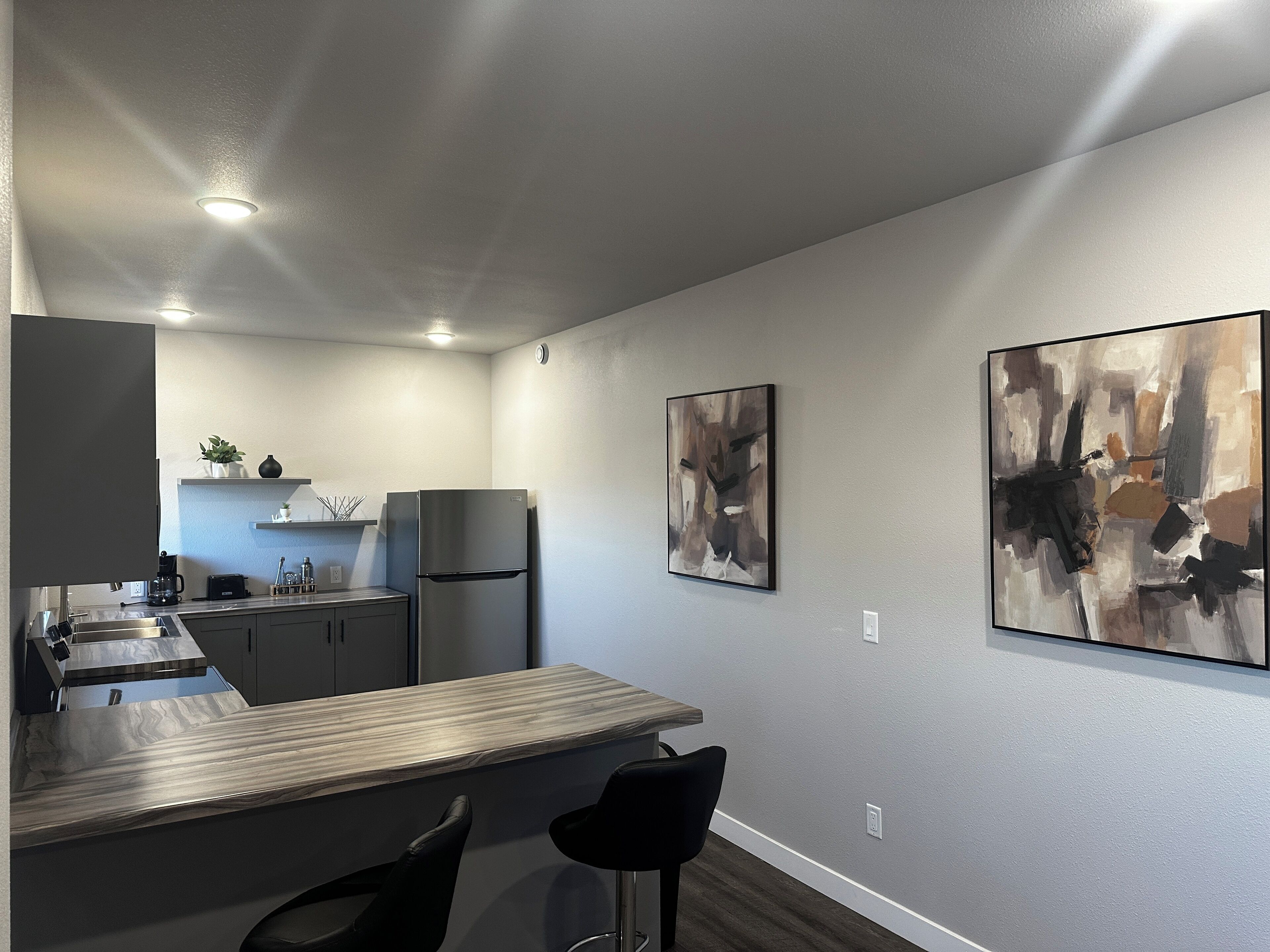 A modern kitchen with a built-in refrigerator, a coffee maker, and a bar area with two stools.