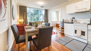 A modern kitchen with white cabinets, a stove, and a microwave. There is a dining area with a wooden table and chairs, and a sofa. - Auchenflower 1BR Retreat, Parking Close to UQ & M5 (Auchenflower)