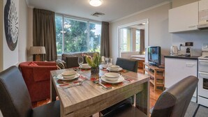 A dining area with a wooden table set for four, a sofa, a TV, and a kitchen area with a microwave and coffee maker. - Auchenflower 1BR Retreat, Parking Close to UQ & M5 (Auchenflower)