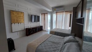A modern hotel room with two beds, a flat-screen TV mounted on the wall, and a large window with sheer curtains. - Casa Blanca Grand (Acapulco de Juárez)