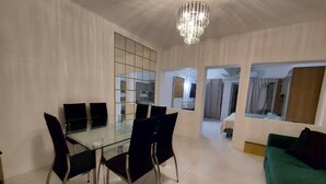 A modern living room with a glass dining table, black chairs, a green sofa, and a chandelier. - Casa Blanca Grand (Acapulco de Juárez)