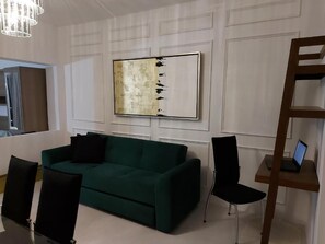 A modern living room with a green sofa, black chairs, a wooden side table with a laptop, and a large abstract painting on the wall. - Casa Blanca Grand (Acapulco de Juárez)
