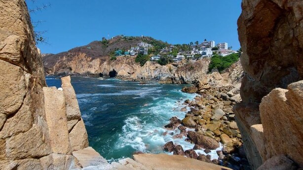 A coastal view with rocky terrain and buildings on a hillside. - Casa Blanca Grand (Acapulco de Juárez)
