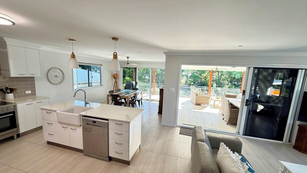 A modern kitchen with a central island, a dining area with outdoor seating, and a sliding glass door leading to a balcony.
