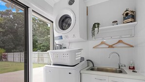 A compact laundry room with a built-in washer and dryer, a sink, and a small shelf with a plant and a basket.