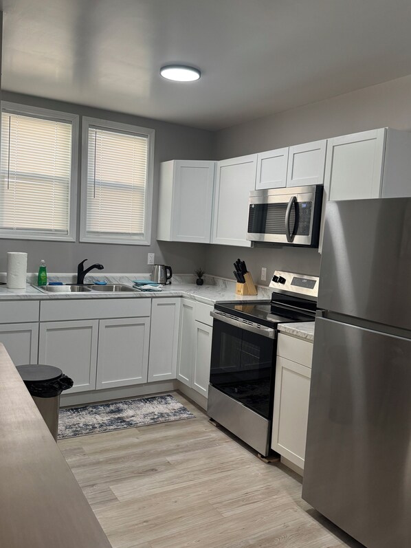 A modern kitchen with white cabinets, stainless steel appliances, a microwave, oven, and a refrigerator.