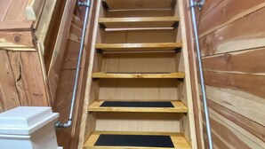 Una escalera de madera con barandales de metal que conduce a una zona superior con una puerta blanca y un ventanal.